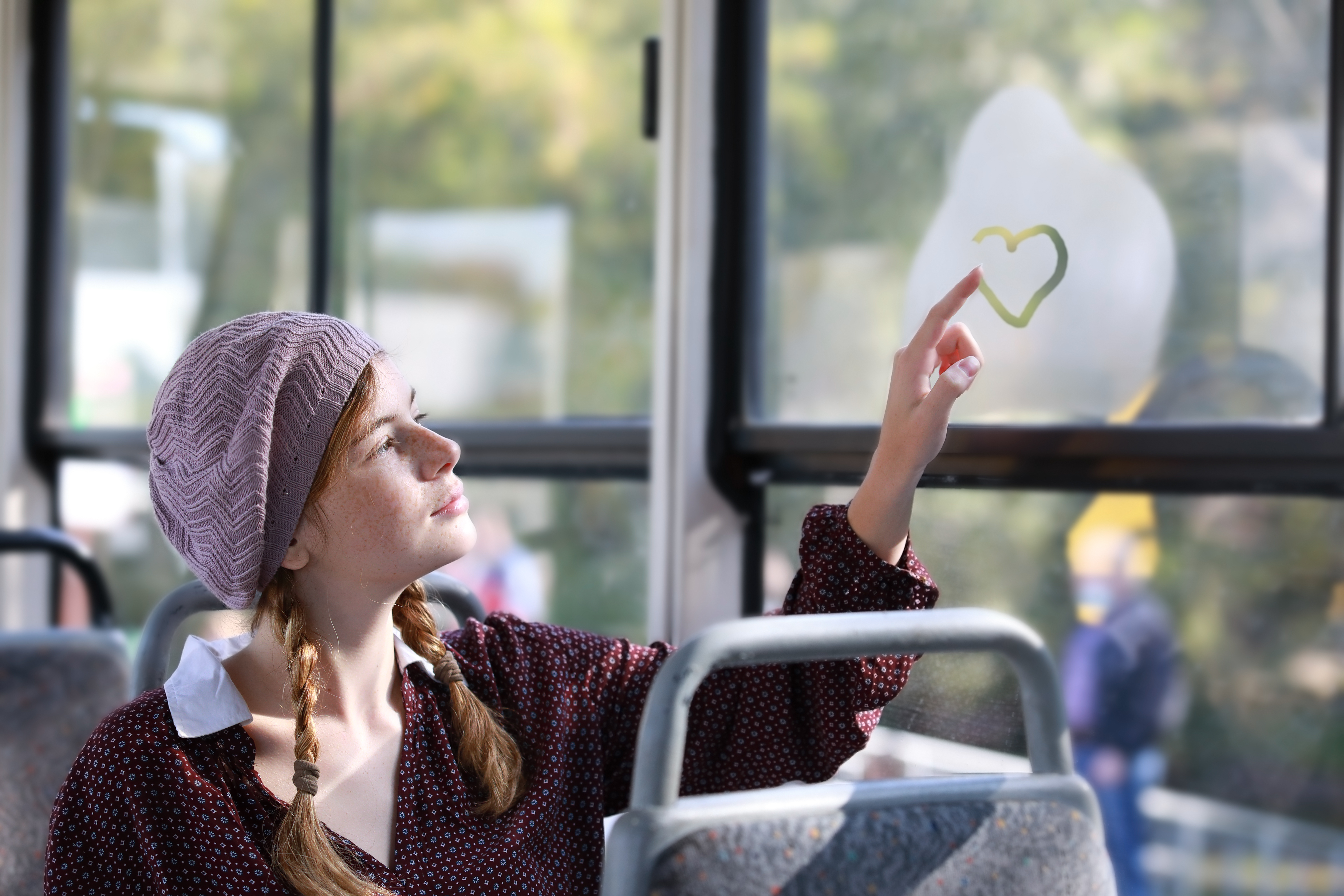 Young girl in retro style clothes draws a heart on a window of t